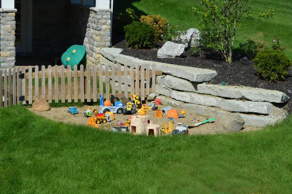 Natural stone wall and boulder transition beside lawn, planting, and a small fenced play area.